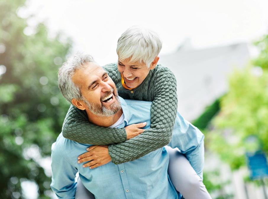 A happy older couple, the man giving the woman a piggyback ride, both laughing joyfully.