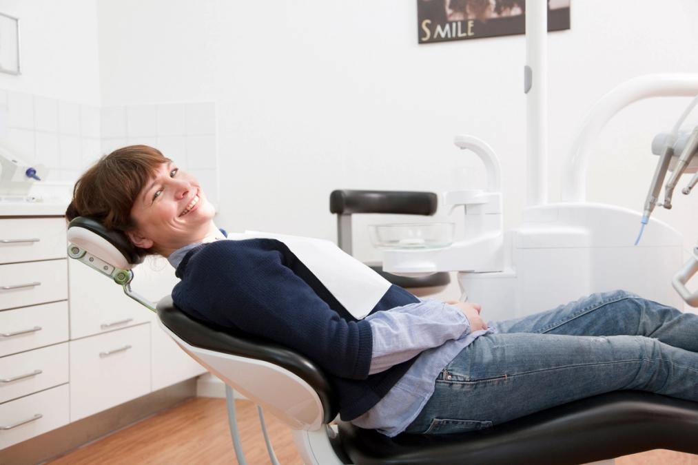 A smiling woman reclines in a dental chair in a bright office.