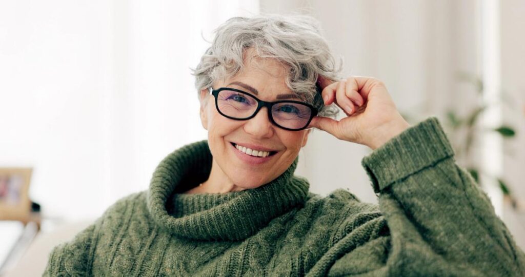 Smiling older woman with short gray hair, glasses, and a green sweater.