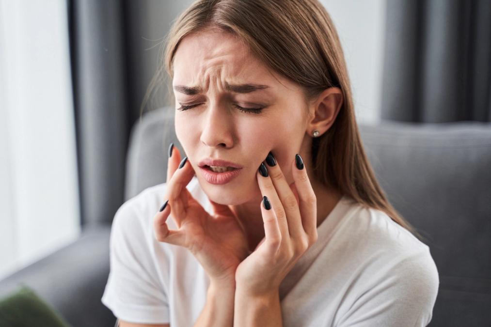 A woman grimaces, holding her jaw in pain.