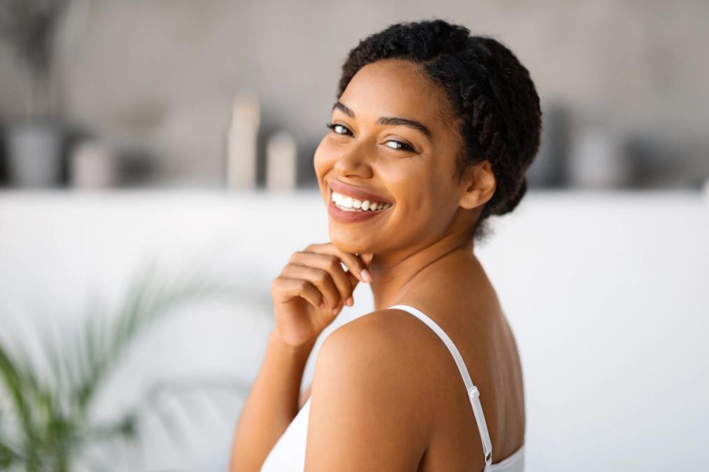 A smiling woman in a white camisole looks over her shoulder.