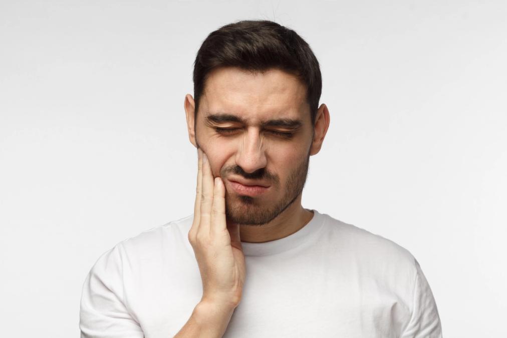 Man with a pained expression holding his jaw, indicating toothache or jaw pain.