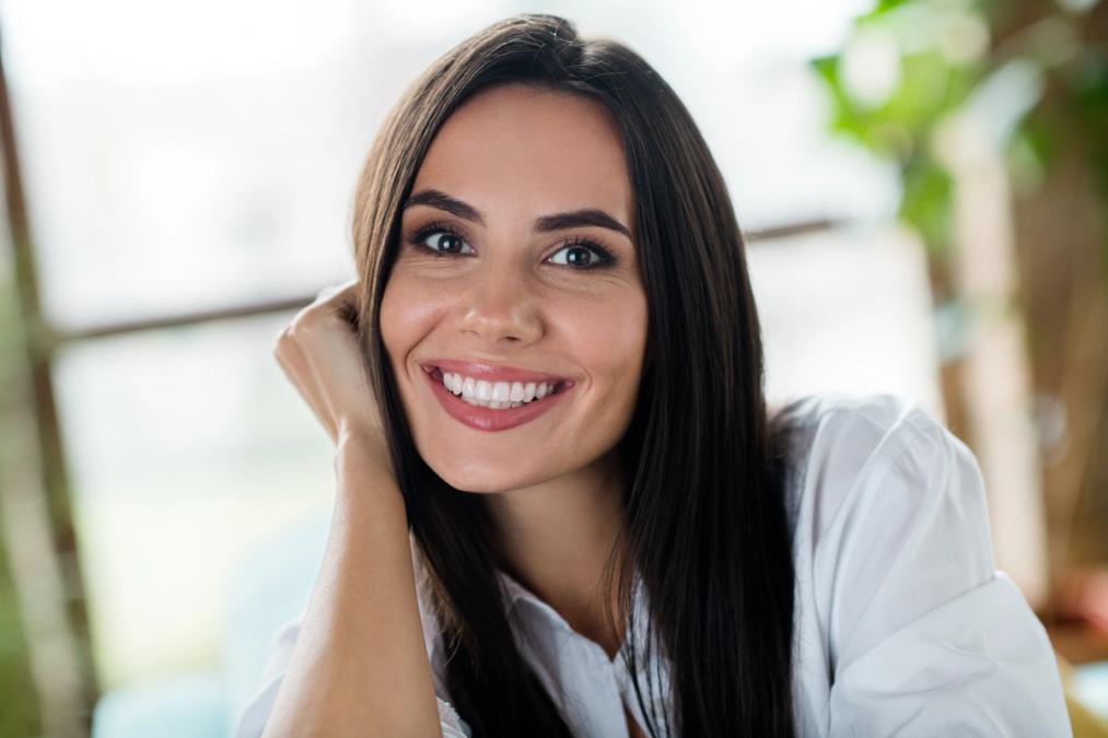 A smiling woman with long dark hair rests her chin on her hand.