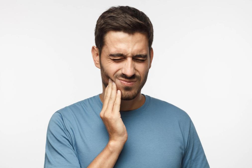 Man grimacing and holding his jaw in pain.